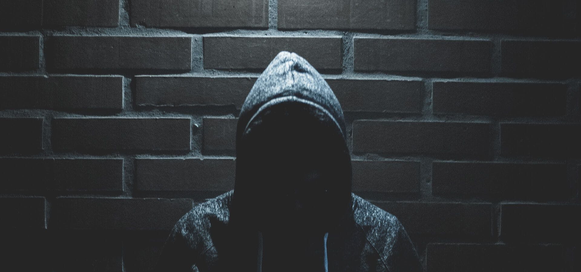 Hacker a oscuras apoyado en una pared de ladrillos